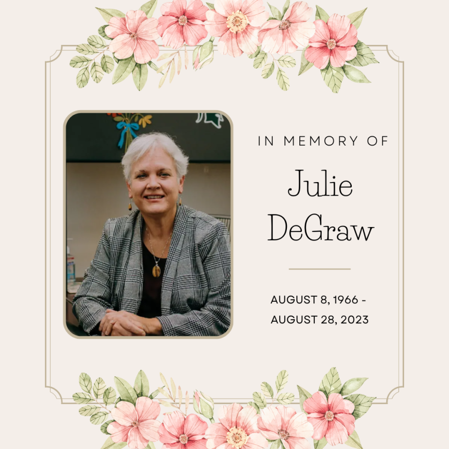 Light pink background with pink flowers that adorn the top and bottom borders. Julie's picture is on the left; she is sitting at a desk, wearing a black top and gray blazer. She has short, white hair and her arms are crossed in front of her on top of the desk and is smiling. To the right of the photo is the copy, "In Memory of Julie DeGraw" "August 8, 1966 - August 28, 2023"