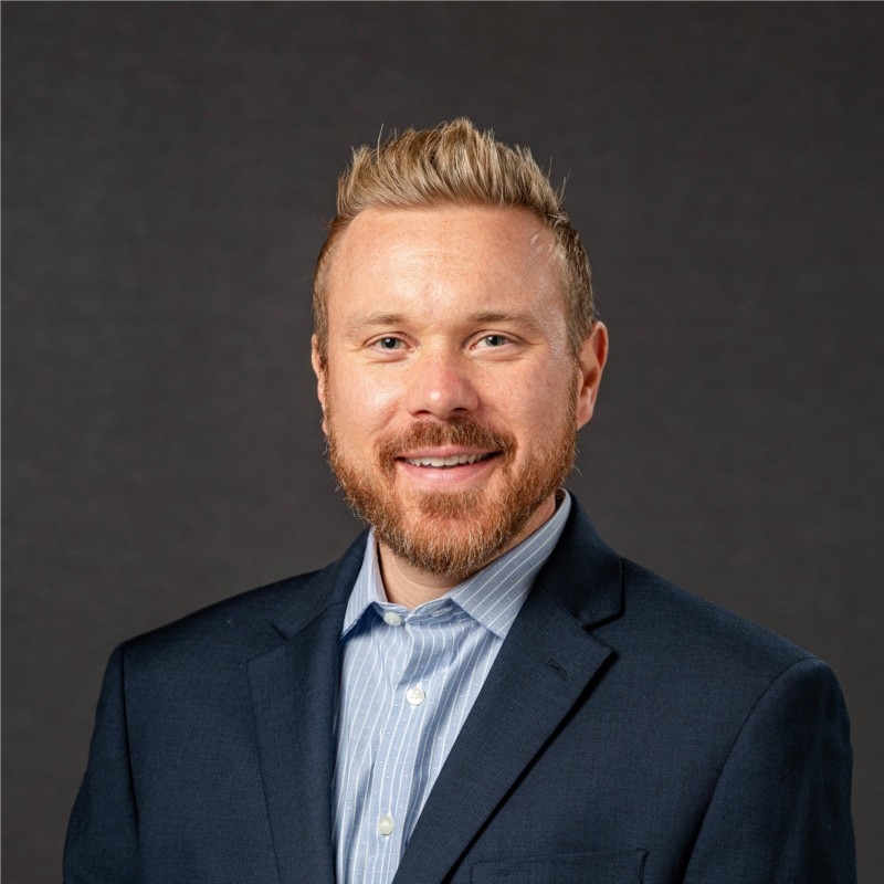 Photo of Allen smiling and wearing a dark navy suit coat with a light blue button-down shirt. He has short, blonde and spikey hair with a full beard.