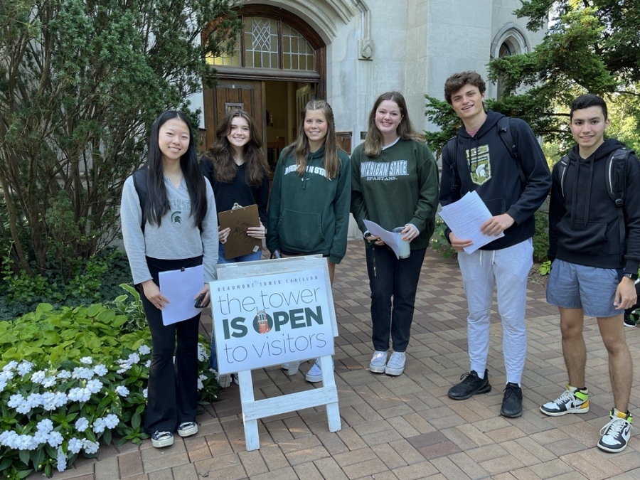 6 students standing in front of a sign near Beaumont Tower's door saying "the tower is open to visitors" and giving tower tours