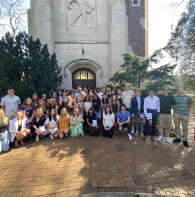Group of 75 students wearing bright, professional clothes standing in front of Beaumont Tower smiling at the camera on a sunny day
