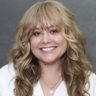 Headshot of Colleen Floyd, a white woman with long, wavy blonde hair. She is smiling at the camera and wearing a white shirt.