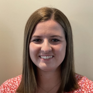 Photo of Katherine West: A woman with long brown hair, wearing a red floral shirt.